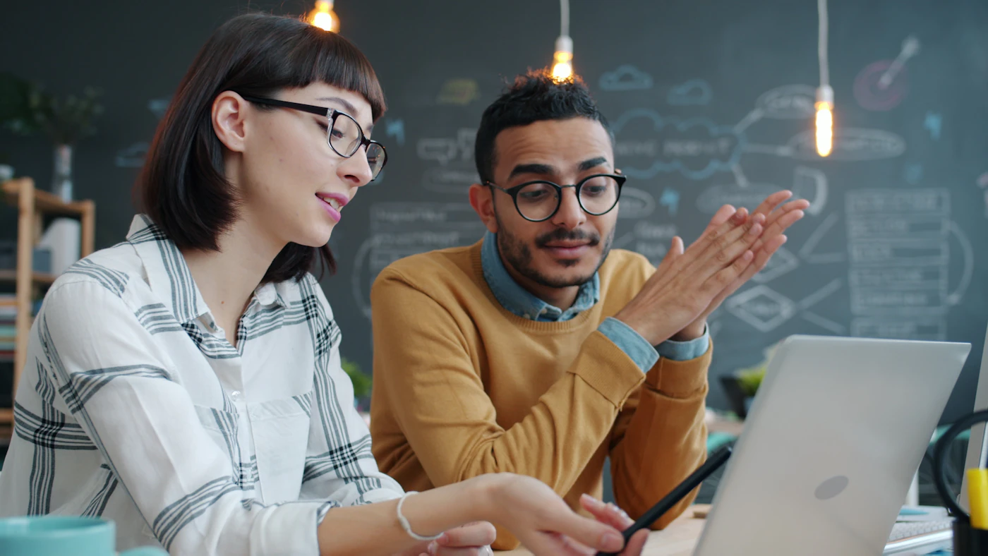 Coworkers discussing a project around a laptop in a studio office